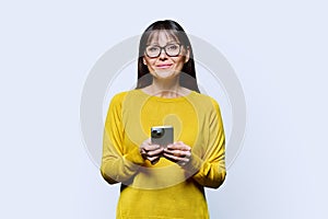 Middle aged smiling woman using smartphone on white studio background