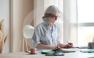 Middle aged stylish woman fashion designer drawing sketches in studio office.