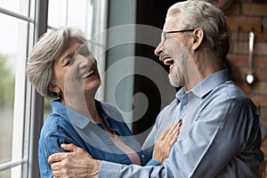 Middle-aged untroubled couple hugging laughing while standing indoor