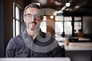 Middle aged white male creative sitting in an office smiling to camera, head and shoulders, close up