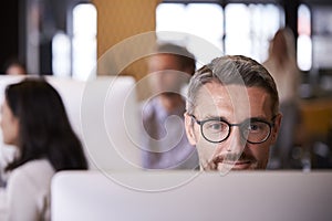 Middle aged white male creative using a computer in a busy office, selective focus, close up