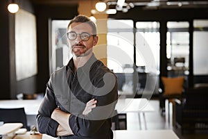 Middle aged white male creative wearing glasses standing in an office looking to camera, waist up