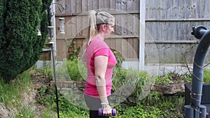 A middle aged white woman doing a mixture of aerobic and anaerobic exercises in her garden