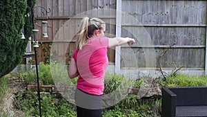 A middle aged white woman doing a mixture of aerobic and anaerobic exercises in her garden