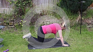 A middle aged white woman doing a mixture of aerobic and anaerobic exercises in her garden