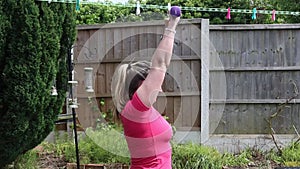 A middle aged white woman doing a mixture of aerobic and anaerobic exercises in her garden