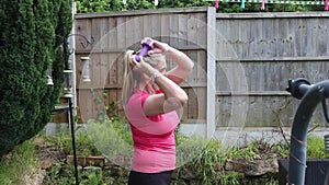 A middle aged white woman doing a mixture of aerobic and anaerobic exercises in her garden