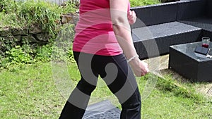 A middle aged white woman doing a mixture of aerobic and anaerobic exercises in her garden
