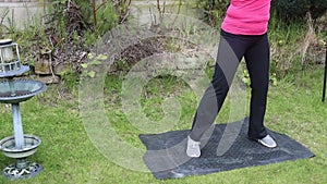 A middle aged white woman doing a mixture of aerobic and anaerobic exercises in her garden