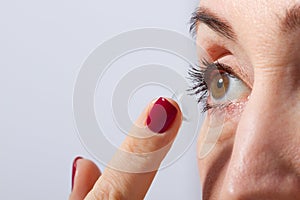 Middle aged woman applying or putting contact lens for vision in her brown eye by finger. Close up and isolated. Selective focus a