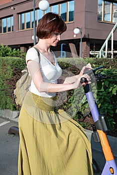 Middle-aged woman with a backpack rents an electronic scooter through a mobile application