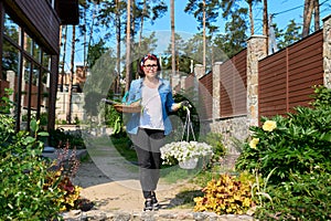 Middle-aged woman in backyard with gardening tools and blooming petunia in pot