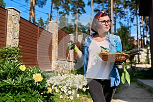 Middle-aged woman in backyard with gardening tools and blooming petunia in pot