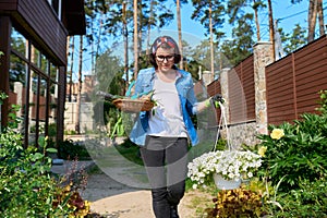 Middle-aged woman in backyard with gardening tools and blooming petunia in pot