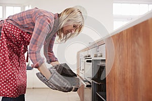 Middle aged woman bending down to take food out of the oven