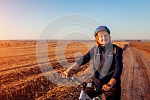 Middle-aged woman bicyclist riding in autumn field at sunset. Senior sportswoman enjoying hobby.