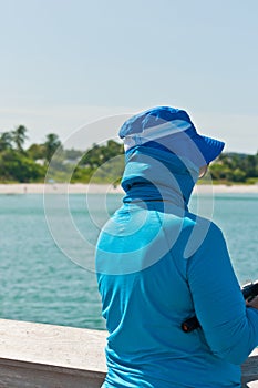 Middle aged woman in blue hat and cloths, fishing from wood pier