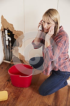 Middle aged woman with burst pipe phoning for help, vertical