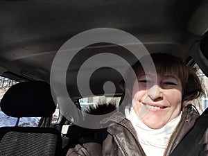 Middle aged woman in a car taking selfie while enjoying a drive. Female mature driver posing inside car. Funny happy