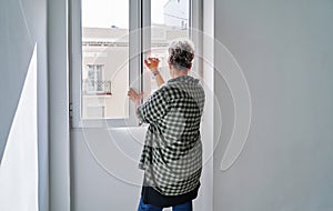 Middle-aged woman closing the window in a room at home