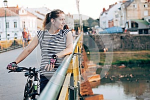 A middle-aged woman while cycling stopped at a pedestrian bridge across the river and admiring the sunset