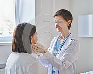 Middle-aged woman doctor wearing gloves checking patients sore throat or thyroid glands