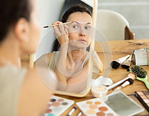 Middle-aged woman doing eyebrow make-up looking in the mirror