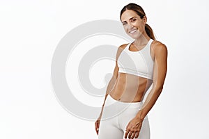 Middle aged woman doing fitness workout, standing in activewear with abs and muscles, smiling happy, standing over white