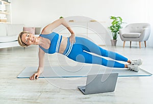 Middle-aged woman doing side plank on mat with pc