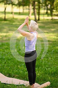Middle-aged woman doing yoga outdoors in the park in Tadasana pose.Mountain Pose. Samasthiti.Back view