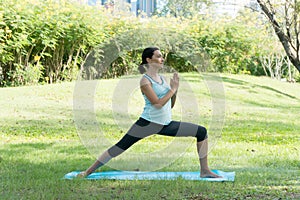 Middle-aged woman doing Yoga in the parks. Female standing on Yoga mat on the grass in the park exercises outdoors.