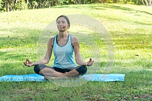 Middle-aged woman doing Yoga in the parks. Female standing on Yoga mat on the grass in the park exercises outdoors.