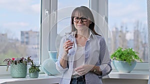 Middle aged woman drinking glass of water, smiling looking at camera