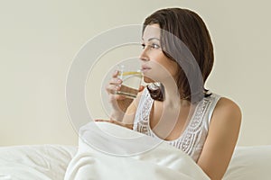 Middle-aged woman enjoys water with a lemon sitting in bed. First morning drink, antioxidant drink