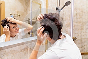 Middle aged woman is examining gray hair in the mirror