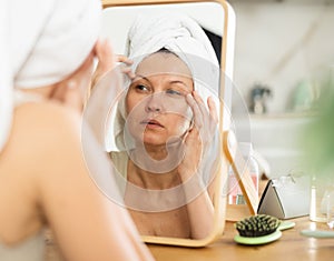 Middle-aged woman examining her facial skin looking in the mirror put on the table