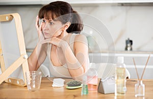 Middle-aged woman examining her facial skin looking in the mirror put on the table