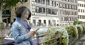 Middle-aged woman in glasses traveler using the application on a smartphone, stay in the old town, next to the river