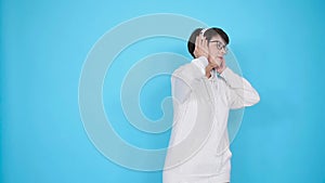 Middle-aged woman in glasses and a white sweater listens to her favorite music with headphones on a white background