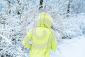 Middle aged woman in green sportswear running in winter snow park. Happy fit middle aged woman trail running in the