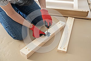 Middle aged woman hands assembling furniture at home. Woman using screwdriver while sitting on floor in apartment and