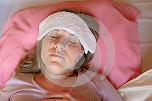 Middle aged woman has a fever or abnormal blood pressure. 40 years women lying in the bed with wet compress on a head. She is