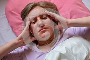 Middle aged woman has a headache. 40 years women lying in the bed and touches the head with hands. She is unwell and sick. Girl