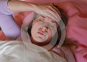Middle aged woman has a high temperature. 40 years women lying in the bed and touches the forehead with hand. She is unwell and