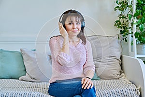 Middle-aged woman in headphones listening to audio, music, audiobook, communication