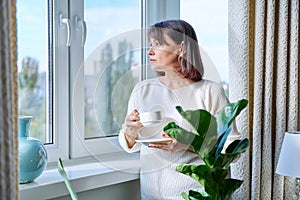 Middle aged woman at home near the window with a cup of coffee