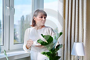 Middle aged woman at home near the window with a cup of coffee