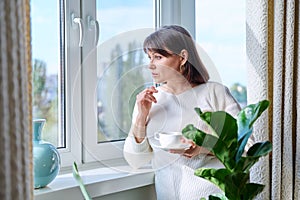 Middle aged woman at home near the window with a cup of coffee