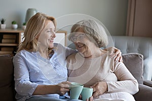 Middle-aged woman hugs older mum drink tea and talking