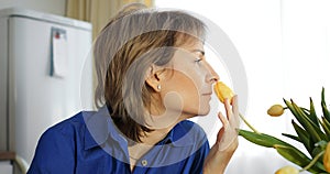 Middle-aged woman inhales yellow tulip scent. Flower fragrance, natural aromatherapy moment, Gen X. Flowers essence